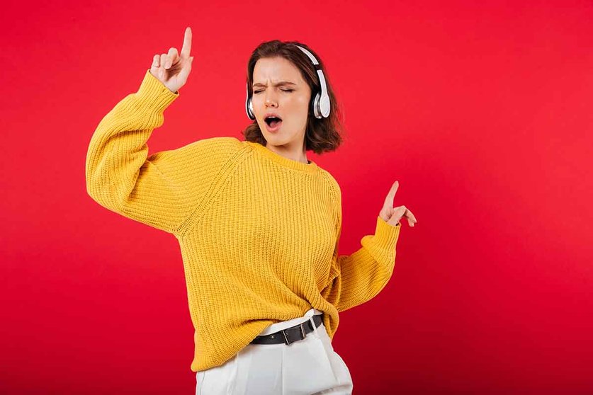 Portrait of a cheerful woman in headphones listening to music and dancing isolated over pink background